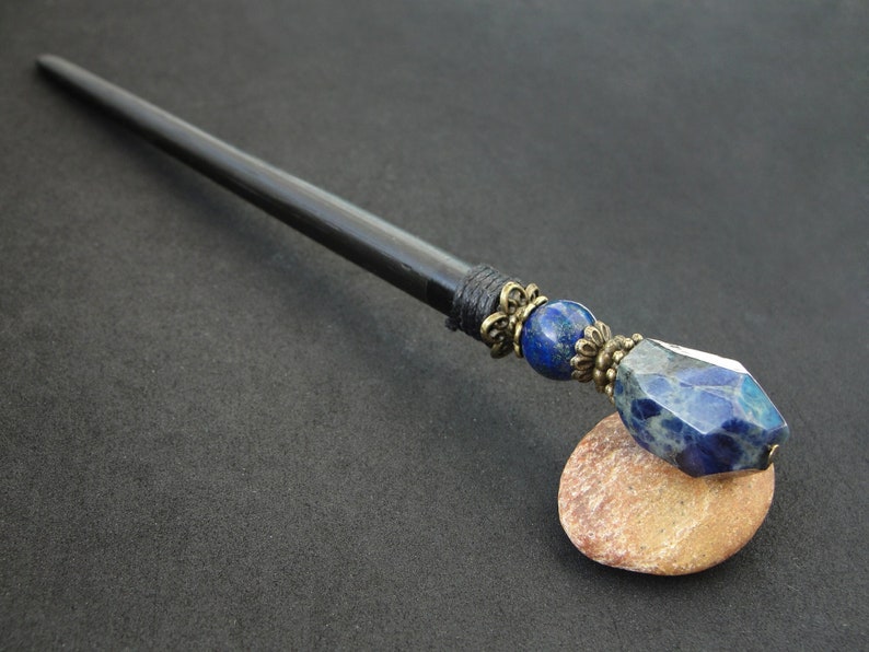May include: Black wooden hair stick with a blue and silver gemstone and a decorative metal accent.