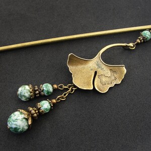 Puede incluir: Una varita para el pelo dorada con un dise&ntilde;o de hoja de ginkgo y cuentas de &aacute;gata verde. La varita mide aproximadamente 25 cm de largo.