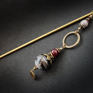 May include: A gold hair stick with a black and white agate bead, a red bead, and a decorative circle charm.