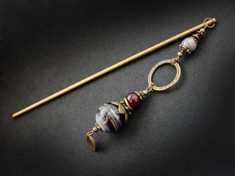 May include: A gold hair stick with a black and white agate bead, a red bead, and a decorative circle charm.