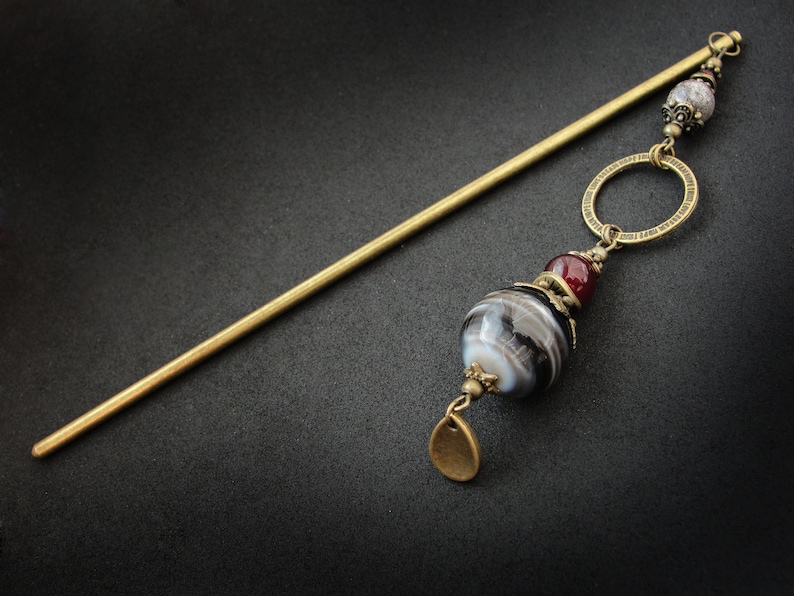 May include: A gold hair stick with a black and white agate bead, a red bead, and a gold ring. The stick is about 12 inches long.