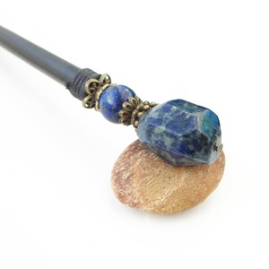 May include: A black wooden hair stick with a blue gemstone and brass accents.