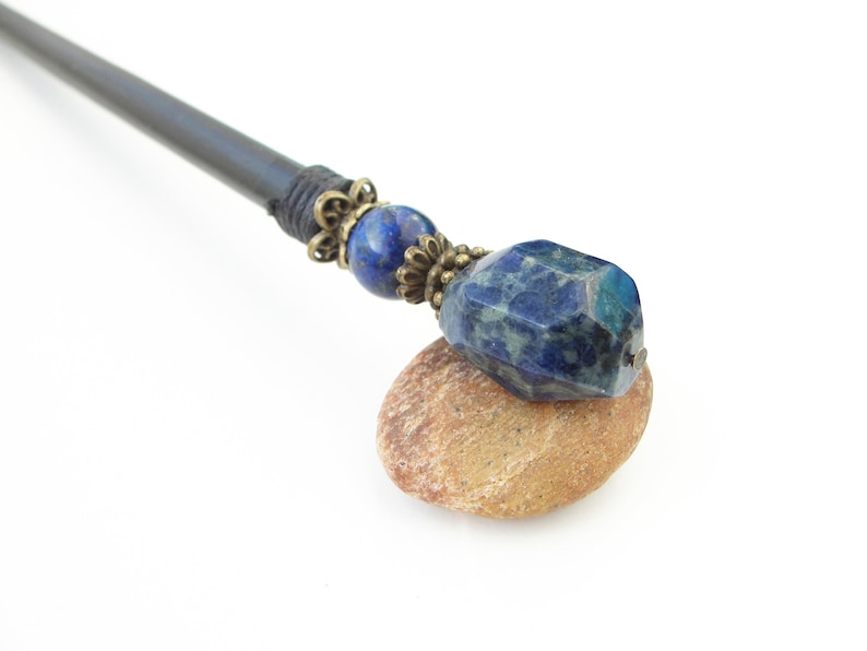 May include: A black wooden hair stick with a blue gemstone and brass accents.