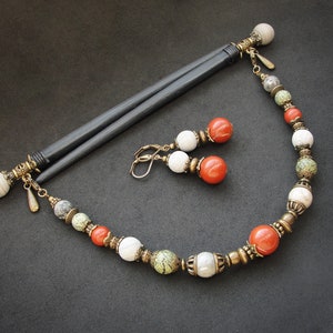 Könnte beinhalten: Ein Set aus Haarnadeln und Ohrringen mit einer Perlenkette. Die Haarnadeln sind schwarz mit weißen und goldenen Akzenten. Die Ohrringe sind golden mit weißen und roten Perlen. Die Kette besteht aus weißen, roten und grünen Perlen mit goldenen Akzenten.