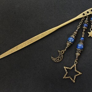Puede incluir: Una varita para el pelo dorada con colgantes, incluyendo estrellas, medias lunas y cuentas de lapisl&aacute;zuli azul.