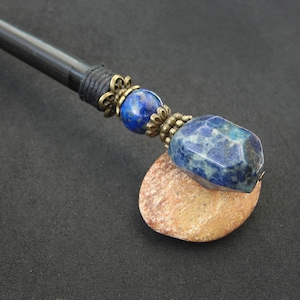 May include: A black wooden hair stick with a blue and white gemstone and gold-toned metal accents.