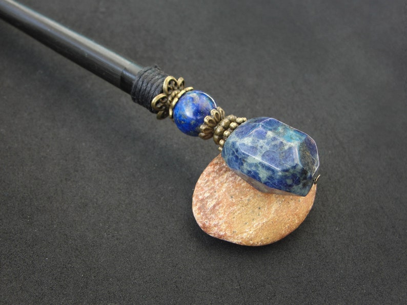 May include: A black wooden hair stick with a blue and white gemstone and gold-toned metal accents.