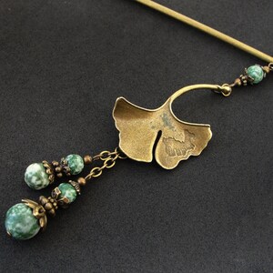 Puede incluir: Una varita para el pelo de tono dorado con un dise&ntilde;o de hoja de ginkgo y cuentas de &aacute;gata verde. La varita est&aacute; decorada con peque&ntilde;as cuentas y una cadena.