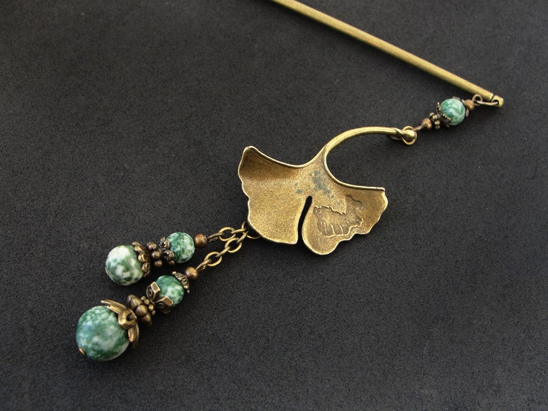 Puede incluir: Una varita para el pelo de tono dorado con un dise&ntilde;o de hoja de ginkgo y cuentas de &aacute;gata verde. La varita est&aacute; decorada con peque&ntilde;as cuentas y una cadena.