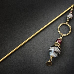 May include: A gold hair stick with a decorative circle and a large, round, black and white agate bead with a red bead above it.
