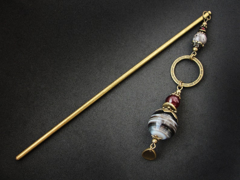 May include: A gold hair stick with a decorative circle and a large, round, black and white agate bead with a red bead above it.