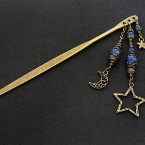 Puede incluir: Una varita para el pelo dorada con cuentas de lapisl&aacute;zuli azul, un amuleto de luna creciente y un amuleto de estrella. La varita mide aproximadamente 30 cm de largo.