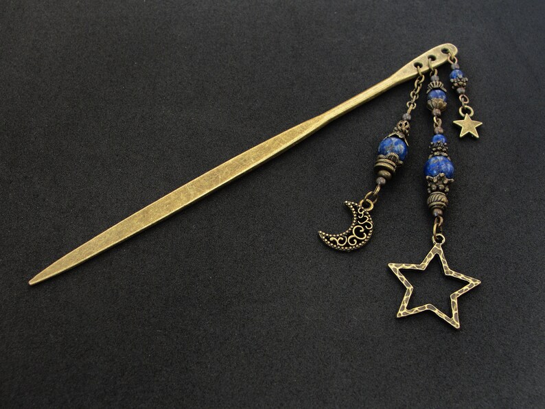 Puede incluir: Una varita para el pelo dorada con cuentas de lapisl&aacute;zuli azul, un amuleto de luna creciente y un amuleto de estrella. La varita mide aproximadamente 30 cm de largo.