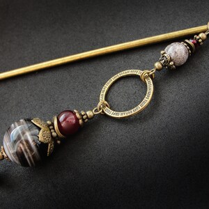 May include: A gold hair stick with a decorative ring and beads. The beads are black and white striped, red, and white with a speckled pattern.