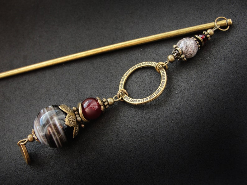 May include: A gold hair stick with a decorative ring and beads. The beads are black and white striped, red, and white with a speckled pattern.