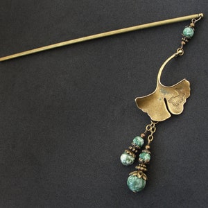 Puede incluir: Una varita para el pelo dorada con un dise&ntilde;o de hoja de ginkgo y cuentas de piedra verde. La varita mide aproximadamente 30 cm de largo.