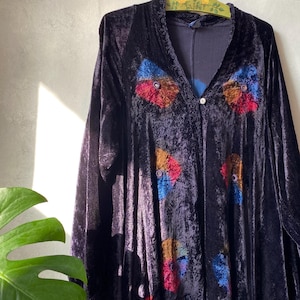 Puede incluir: Una bata de terciopelo azul marino oscuro con mangas largas y cuello en V. La bata presenta aplicaciones circulares coloridas en rojo, naranja, azul y amarillo. Un solo botón abrocha la bata en el pecho.