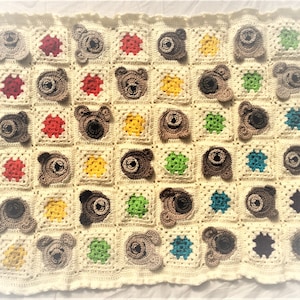 Op de afbeelding: Een gehaakt babydekentje met een witte achtergrond en bruine berenapplicaties. Het dekentje heeft verschillende gekleurde vierkanten met verschillende patronen.