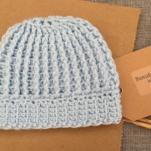 May include: A light blue crocheted baby hat with a ribbed texture. The hat is made by BeautiWool Handcrafts, Melbourne, Australia.