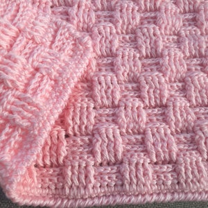 May include: Close-up of a pink crocheted blanket with a woven pattern.