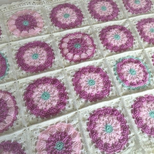 May include: A crocheted baby blanket with a white background and pink and green floral designs.