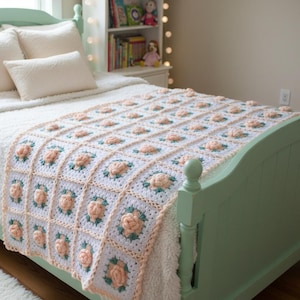 May include: A handmade crochet blanket featuring a repeating square pattern. Each square consists of a white border surrounding a central three-dimensional peach-colored rose with green leaves, all joined together to form a textured bed covering.