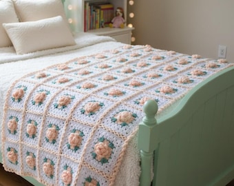 May include: A handmade crochet blanket featuring a repeating square pattern. Each square consists of a white base with a three-dimensional peach-colored rose flower in the center, accented by small green leaves. The blanket has a peach-colored border.