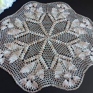Könnte beinhalten: Handgefertigte Häkeldecke in Creme mit detailliertem Blumenmuster. Die Decke hat einen gewellten Rand und ein zentrales Sternmuster. Die filigrane Lochmusterung erzeugt eine zarte und Vintage-Ästhetik für die Heimdekoration.