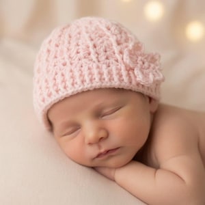 May include: A light pink crochet baby hat featuring a textured ribbed pattern and a decorative crocheted flower accent on the side. The hat is constructed with a soft yarn material and has a rounded shape that fits snugly around the head.