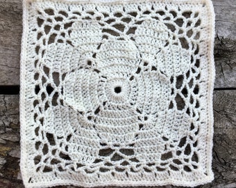 Könnte beinhalten: Ein weißes gehäkeltes Quadrat mit einem runden Design in der Mitte. Das Quadrat hat ein zartes, durchbrochenes Muster.