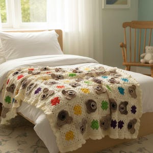 May include: A cream-coloured crochet blanket featuring a repeating pattern of brown bear faces and small, solid-coloured squares in bright red, yellow, green, and purple. The blanket has a scalloped edge and is draped over a white bedspread.
