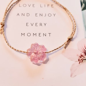 Könnte beinhalten: Ein Armband mit einem rosa Blumenanhänger mit der Aufschrift "Love life and enjoy every moment".