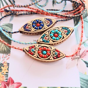 May include: Three decorative eye-shaped bracelets with colorful mosaic designs. Each bracelet features a central design with red, blue, and turquoise accents, set in a gold-colored frame. The bracelets are strung on braided cords in shades of blue, red, and gold.