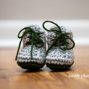 May include: A pair of gray crocheted baby booties with green laces. The booties have a green trim around the bottom.