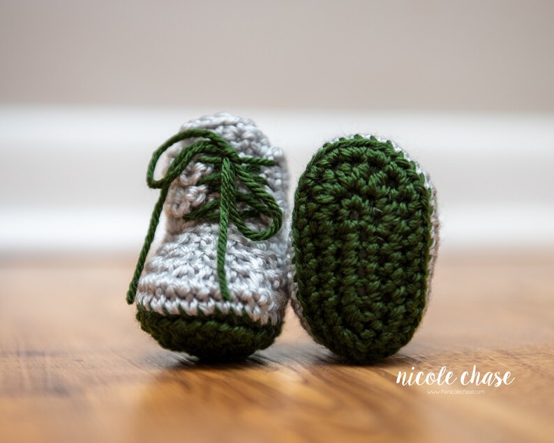 May include: A pair of crocheted baby booties with green and gray yarn. The booties have laces and a green sole.