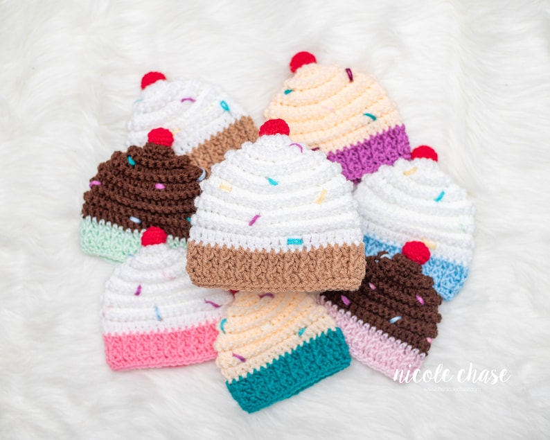 Peut inclure: Un ensemble de sept bonnets en crochet en forme de cupcake dans diff&eacute;rentes couleurs, notamment le blanc, le marron, le rose, le bleu et le jaune. Chaque bonnet pr&eacute;sente un motif de gla&ccedil;age blanc avec des p&eacute;pites color&eacute;es et une cerise rouge sur le dessus.
