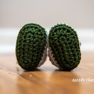 May include: A pair of green and gray crocheted baby booties. The booties have a textured pattern and are made with soft yarn.