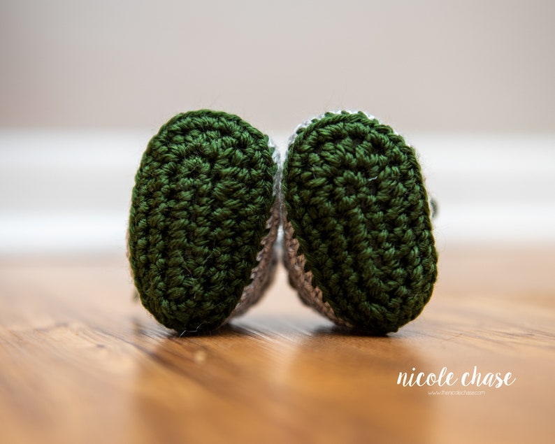 May include: A pair of green and gray crocheted baby booties. The booties have a textured pattern and are made with soft yarn.