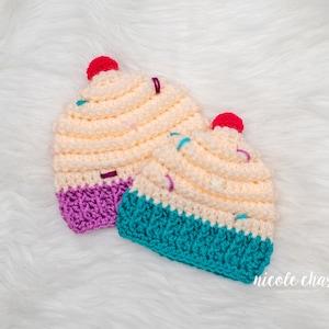 Peut inclure: Deux bonnets en crochet en forme de cupcake, l'un avec un gla&ccedil;age violet et l'autre avec un gla&ccedil;age turquoise. Les deux bonnets ont un motif de p&eacute;pites blanches et roses.
