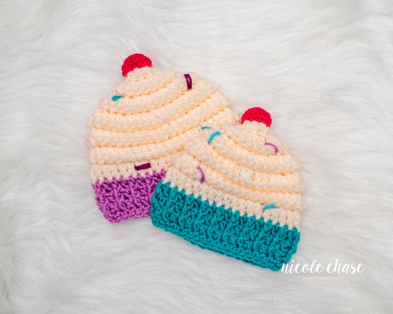 Peut inclure: Deux bonnets en crochet en forme de cupcake, l'un avec un gla&ccedil;age violet et l'autre avec un gla&ccedil;age turquoise. Les deux bonnets ont un motif de p&eacute;pites blanches et roses.
