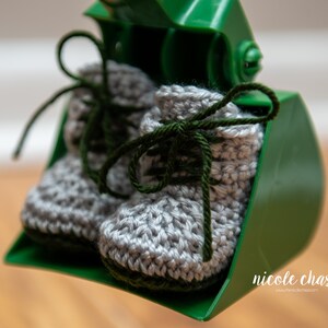 May include: A pair of gray crocheted baby booties with green laces. The booties are sitting in a green plastic scoop.