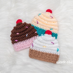 Peut inclure: Trois bonnets en crochet en forme de cupcake dans diff&eacute;rentes couleurs et designs. Les bonnets sont marron, blanc et jaune clair avec des p&eacute;pites et une cerise sur le dessus.