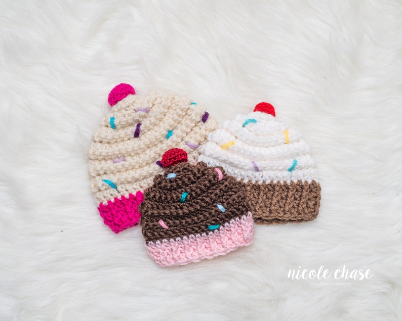 Peut inclure: Trois bonnets en crochet en forme de cupcake dans diff&eacute;rentes couleurs et designs. Les bonnets sont blancs, bruns et beiges avec un gla&ccedil;age rose, blanc et brun et des p&eacute;pites color&eacute;es.