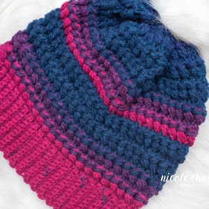 May include: A crocheted beanie hat with a striped pattern in shades of pink and blue. The hat is made with a textured stitch that gives it a puffy look.