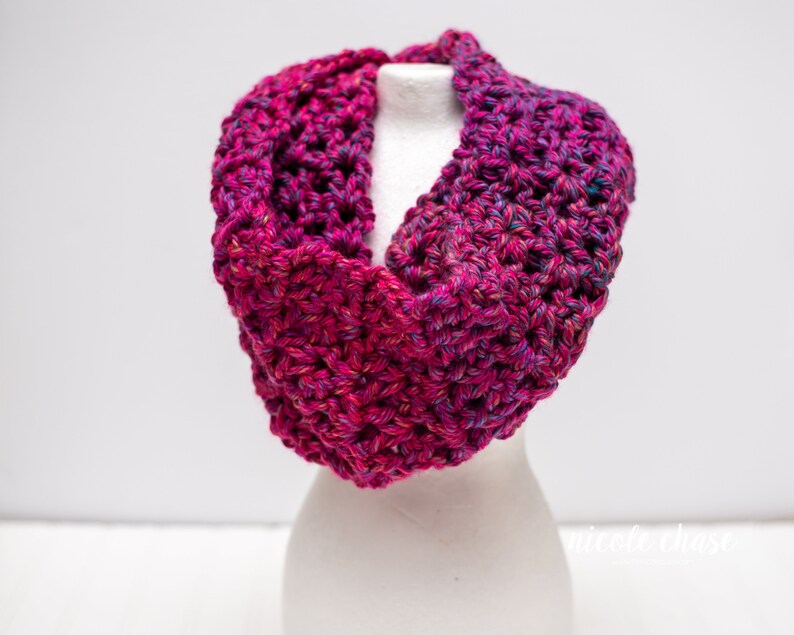 K&ouml;nnte beinhalten: Ein geh&auml;kelter Infinity-Schal in einem tiefen Pink- und Lila-Ombre-Farbverlauf. Der Schal ist aus einem dicken Garn gefertigt und hat ein strukturiertes Stichmuster.