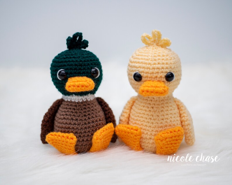 May include: Two crocheted duck plushies, one green and brown and one yellow. Both have black eyes and orange beaks.