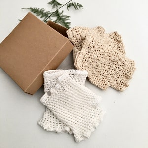 Peut inclure: Deux paires de mitaines en crochet, une paire est blanche et l'autre beige. Les mitaines sont emball&eacute;es dans une bo&icirc;te en carton marron.