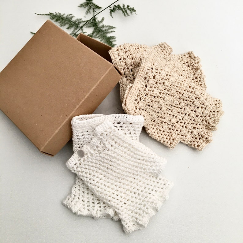 Peut inclure: Deux paires de mitaines en crochet, une paire est blanche et l'autre beige. Les mitaines sont emball&eacute;es dans une bo&icirc;te en carton marron.