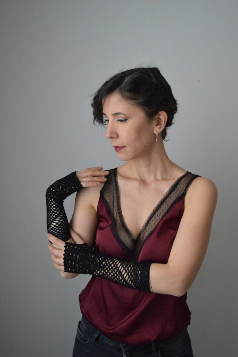 May include: A woman wearing a burgundy satin top with black lace trim and black fishnet fingerless gloves.