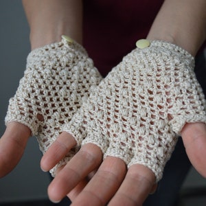Peut inclure: Une paire de mitaines en crochet beige avec un bouton sur chaque poignet.